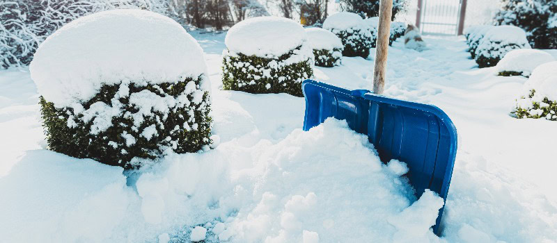 Verschneiter Winter - blaue Schaufel beim Schneeräumen auf dem Gehweg